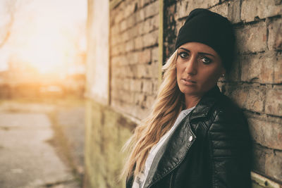 Fashionable young woman wearing jacket standing against brick wall