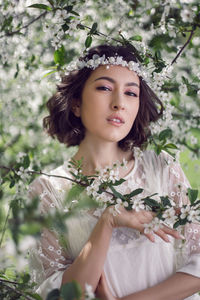 Portrait of a young beautiful woman in white clothes standing next to blooming cherry tree in spring