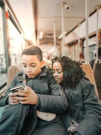 Brother using mobile while sister looking at it