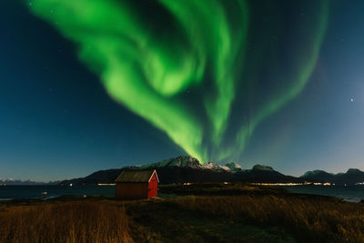 Scenic view of red building against snowcapped mountains and northern lights at night