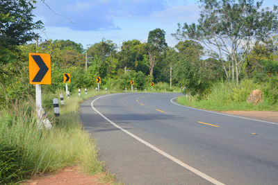 Road sign by trees against sky