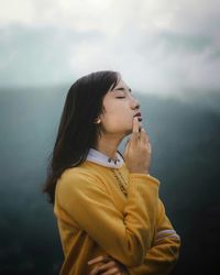 Side view of young woman looking away against sky