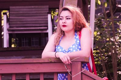 Thoughtful woman looking away while standing by wooden railing