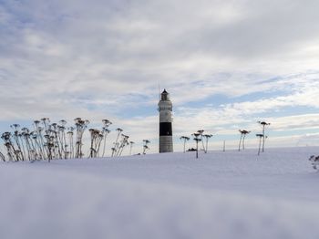 Lighthouse on snow covered land against sky