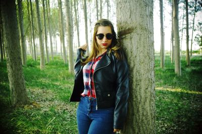 Portrait of woman wearing sunglasses while standing by tree at forest