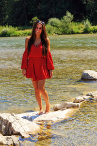 Portrait of smiling young woman standing on rock in river