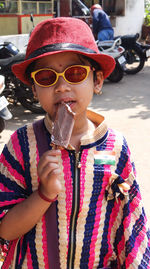 Girl eating popsicle while standing on footpath