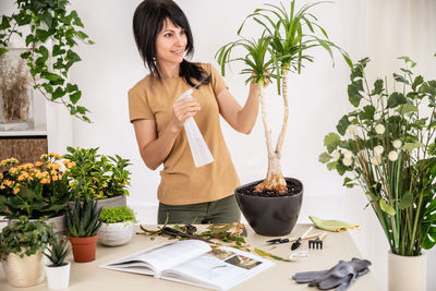 Female gardener watering houseplant using spray bottle working at workshop