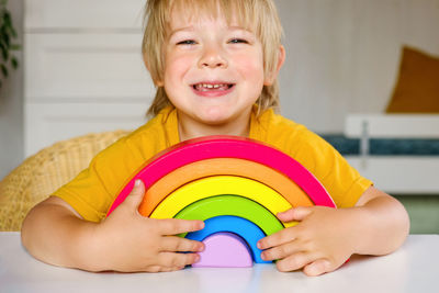 Little blond hair boy in clothes made of natural fabric plays with rainbow colored wooden toys at