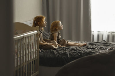 Girl with sister sitting on bed watching tv at home