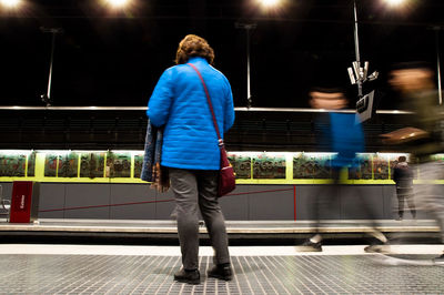 Rear view of woman wearing warm clothing while standing on railroad station platform at night