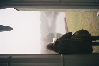 Rear view of woman sitting by car against sky