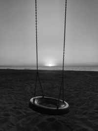 Swing hanging on rope at beach against sky