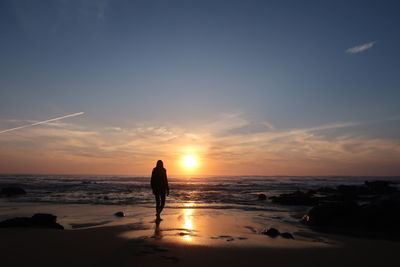 Silhouette man standing on beach against sky during sunset