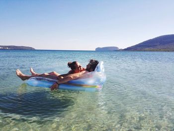 People relaxing in sea against clear sky