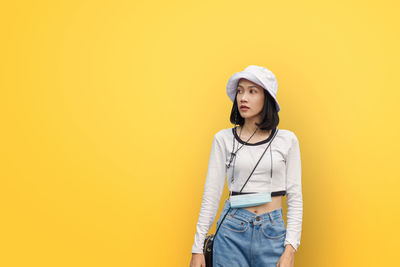 Portrait of young woman standing against yellow background