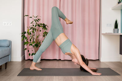 Woman practicing yoga at home, doing the one-legged variation of down dog for stretch side-body. 