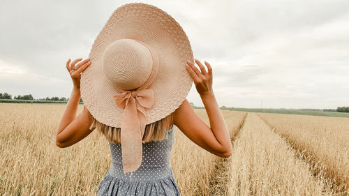 Rear view of woman wearing hat standing on landscape against sky