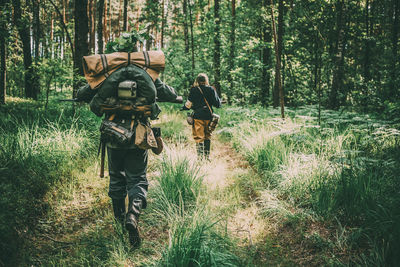 Rear view of army soldiers walking on grassy field amidst trees in forest