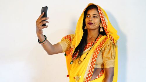 Portrait of young woman holding smart phone against white background