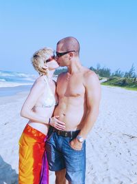 Couple kissing on beach against clear sky