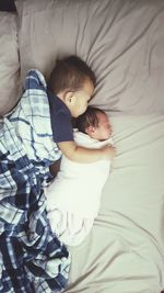 High angle view of boy with newborn brother sleeping on bed at home