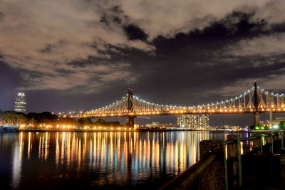 Illuminated bridge over river against sky in city at night