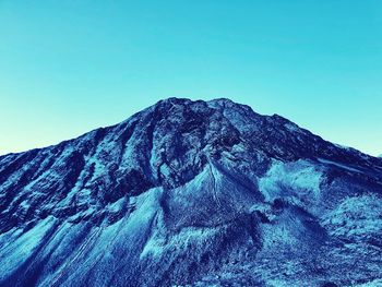 Low angle view of snowcapped mountain against clear blue sky