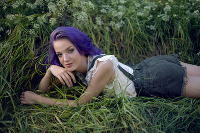 Portrait of a teenage girl with purple hair and an earring in her nose lying in the grass in nature