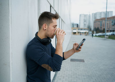 Side view of a modern man in casual clothes sitting near a white wall