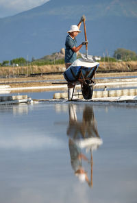 Man working on boat in lake against sky