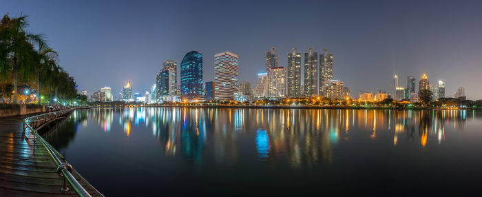 Illuminated buildings by river against sky at night