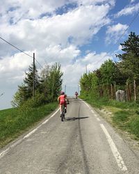 Rear view boy cycling on road against cloudy sky