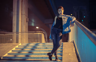 Full length portrait of young man on staircase in city at night