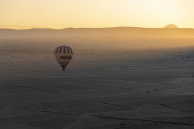 Hot air balloon flying over land against sky during sunset