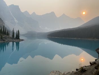 Scenic view of lake by mountains against sky during sunset