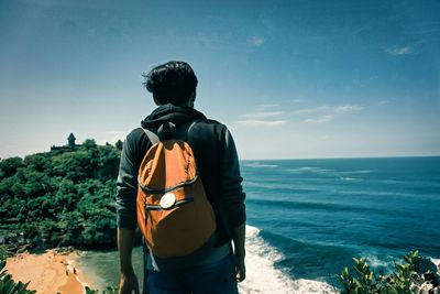 Rear view of man standing facing the sea from the top of the cliff