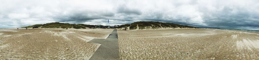 Panoramic view of sandy beach against cloudy sky