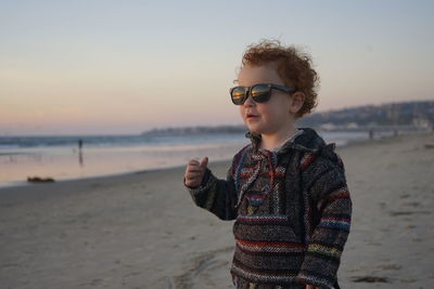 Portrait of boy standing on beach against sky during sunset