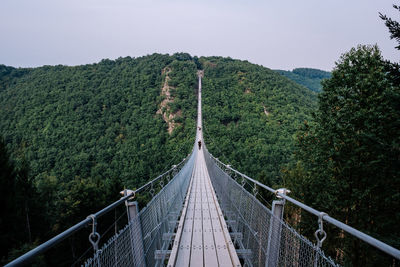 Footbridge amidst trees in forest against clear sky