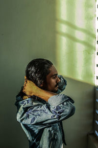 Side view of young man looking away against wall