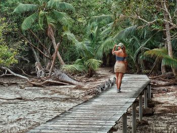 Rear view of woman walking on boardwalk against trees