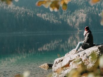 Side view of man sitting on rock by lake