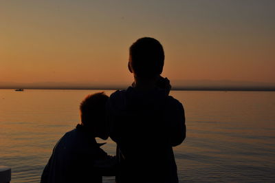 Silhouette couple on sea against sky during sunset