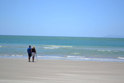 Rear view full length of couple standing on shore at beach against clear sky