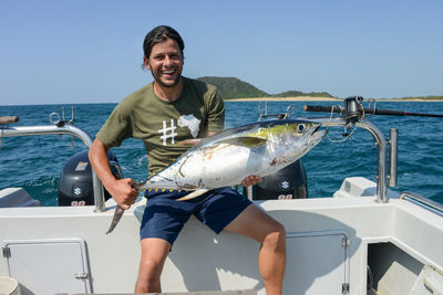 Portrait of smiling man holding fish in boat on sea