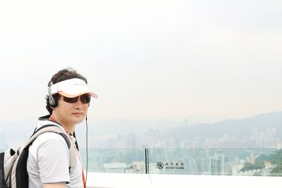 Portrait of man listening to music on terrace against clear sky