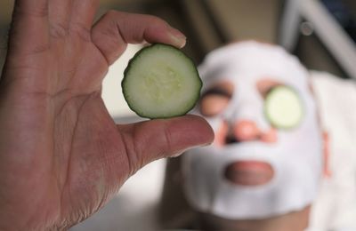 Close-up of man with facial mask on face holding cucumber