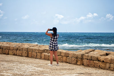 Rear view of woman photographing while standing by sea