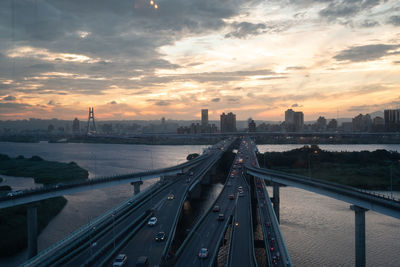 Aerial view of bridge over river by buildings against sky during sunset